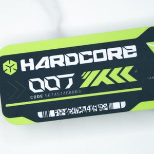 May include: A rectangular black and neon green graphic with the word "HARDCORE" in white, stylized text. Below, the text "DOT" is in white, with a green arrow design. The code "567457468883" is printed below the text. A barcode is at the bottom.