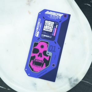 May include: A rectangular, blue and purple card featuring a pink skull graphic and the word "DANGER". The card includes text such as "ROBOTICS" and "NRX-9". The skull graphic has a star in the center and the card has various other text elements.