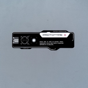 May include: A black rectangular sticker with white technical graphics and text. It features the word PROTOTYPE, a barcode, a circular target icon labeled RESCUE, a sunburst symbol, and text defining a super-capacitor as a device for electric charge.
