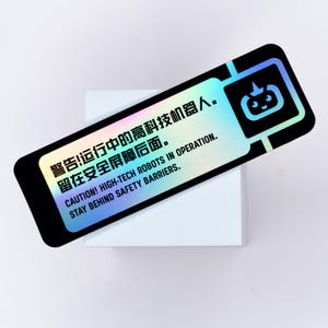 May include: A rectangular sticker with a black border and a holographic background. The sticker features text in English and Chinese, along with a cartoon robot icon. The text warns of high-tech robots in operation and advises staying behind safety barriers.