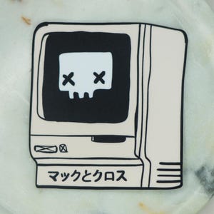 Puede incluir: Una pegatina cuadrada con un dibujo lineal en blanco y negro de un monitor de ordenador antiguo. La pantalla muestra una calavera blanca con ojos en forma de X. Debajo de la pantalla, el texto japonés "マックとクロス" aparece en tinta negra.