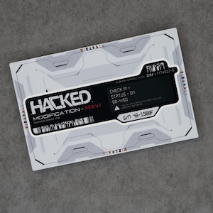 May include: A rectangular card with a white and grey futuristic design. The card features the word "HACKED" in bold black letters, along with other text including "MODIFICATION - R53/a1" and "PROTOCOL DRIVER X138". The card also has a barcode and the text "CHECK IN + STATUS - ON".