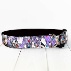 May include: A dog collar with a black interior and a patterned exterior. The pattern features anime-style characters, white speech bubbles, and red hearts on a purple and gray plaid background. The collar has a silver metal D-ring and a black plastic buckle.