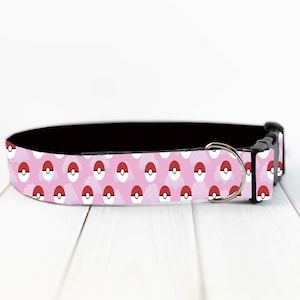 May include: A pink dog collar featuring a repeating pattern of red and white ball designs. The collar has a black interior, a silver metal D-ring, and a black plastic buckle. The collar is designed for pets.