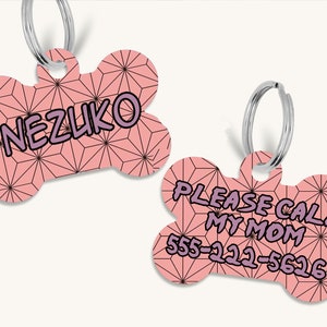 May include: Two pink bone-shaped dog tags with a black and white geometric pattern. The first tag says "NEZUKO" in purple text. The second tag says "PLEASE CALL MY MOM 555-222-5626" in purple text.