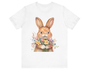 Puede incluir: Camiseta blanca con una ilustración de dibujos animados de un conejo marrón sosteniendo un ramo de flores de colores.