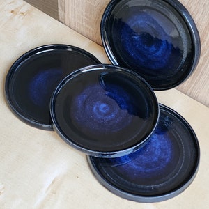 May include: Four black ceramic plates with a blue swirl design. The plates are stacked on top of each other.