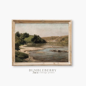 May include: Vintage landscape painting featuring a river scene with a sandy bank and lush green trees. The artwork is framed in a distressed, light-colored wooden frame. The painting has a muted color palette with a soft, natural aesthetic. The text "BUMBLEBERRY home vintage prints" is at the bottom.