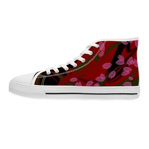 May include: A high-top sneaker featuring a white rubber toe cap, white laces, and a white sole with a thin black stripe. The canvas upper displays a deep red and black abstract swirling background pattern overlaid with scattered pink petal shapes.