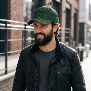 Op de afbeelding: Groene baseballcap met een zwart vizier en een patroon. De cap is gemaakt van een textuurstof en wordt buiten gedragen. De cap is een stijlvol accessoire.