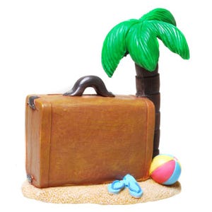 Könnte beinhalten: Ein brauner Vintage-Koffer mit einer Palme, Flip-Flops und einem Strandball auf einem Sandsockel.