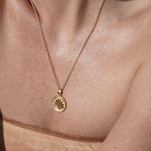 May include: A gold chain necklace with a round pendant featuring a detailed seashell design.