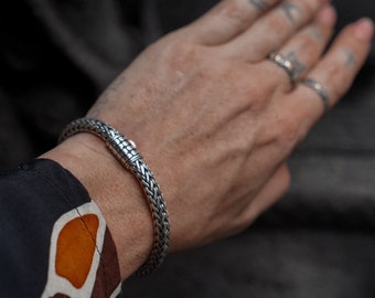 May include: A silver chain bracelet with a clasp closure. The bracelet is on a person's wrist.