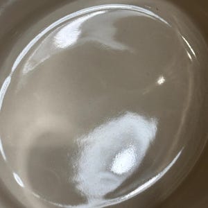 May include: A white ceramic bowl with a smooth, glossy finish. The bowl is empty and has a slight curve to the bottom.