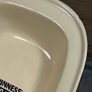 May include: Cream-colored, rectangular serving dish with rounded edges. The dish has a glossy finish and a black and white logo that reads "Guinness Original Stout". The dish is likely made of ceramic or porcelain.