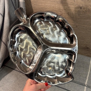 Puede incluir: Una bandeja de servir plateada con tres secciones en forma de hojas. La bandeja tiene un asa en forma de hoja.