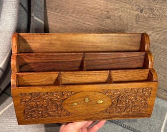 May include: A wooden desk organizer with intricate carvings and brass accents. The organizer has four compartments and is perfect for holding pens, pencils, and other office supplies.