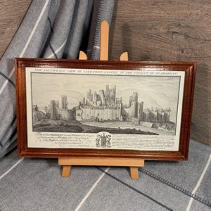 May include: A framed black and white print of a historical illustration depicting Caerphilly Castle in the county of Glamorgan. The print is in a brown wooden frame and includes the text "THE SOUTH-EAST VIEW OF CAER-PHILY-CASTLE, IN THE COUNTY OF GLAMORGAN."