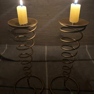 Peut inclure: Deux bougeoirs en m&eacute;tal dor&eacute; avec un design en spirale. Chaque bougeoir a une bougie blanche avec une flamme bleue.