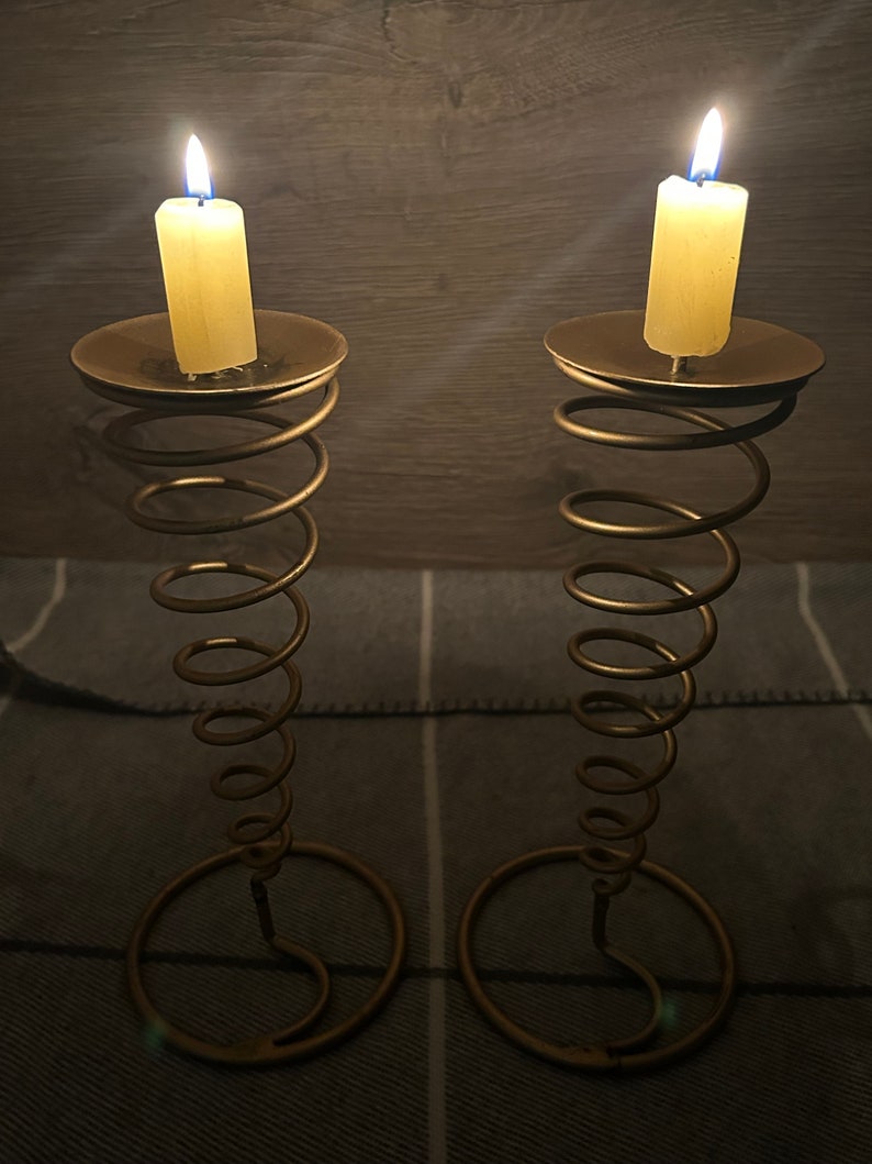 Peut inclure: Deux bougeoirs en m&eacute;tal dor&eacute; avec un design en spirale. Chaque bougeoir a une bougie blanche avec une flamme bleue.