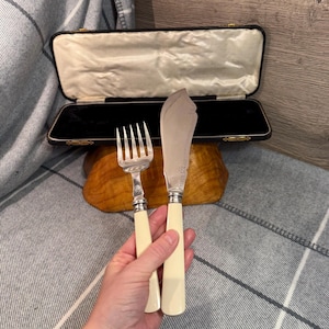 Puede incluir: Un juego de tenedor y cuchillo de mantequilla de plata vintage con mangos de color marfil. El cuchillo tiene un borde decorativo. El juego se presenta con un estuche forrado de terciopelo negro, para una cena formal.