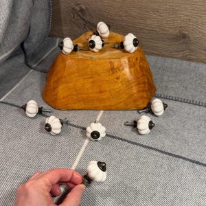 May include: A collection of white ceramic cabinet knobs with a ribbed design and dark bronze-colored hardware. The knobs are arranged on a wooden bowl and a gray patterned surface.