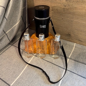 May include: A black leather flask with a zipper closure and the text "Grant's Scotch Whisky". The flask is attached to a black leather strap and is accompanied by four clear glass bottles with silver caps.