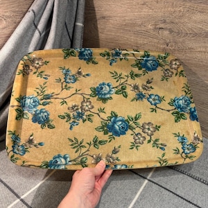 Op de afbeelding: Een rechthoekige serveerschaal met een bloemenpatroon. De schaal heeft een lichtbruine achtergrond met een patroon van blauwe rozen en groene bladeren. De schaal wordt door een persoon vastgehouden.
