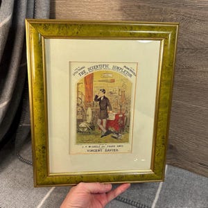 May include: A framed vintage print of a man in a lab coat surrounded by scientific equipment. The print is titled "The Scientific Simpleton" and is by Little Thomas, J.F. Miardle and Frank Amos, composed by Vincent Davies.