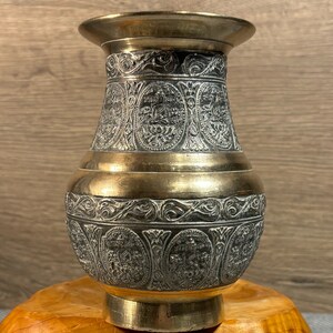 K&ouml;nnte beinhalten: Eine Messingvase mit einem komplizierten, gravierten Design. Die Vase ist dunkelgrau mit goldenen Akzenten. Sie hat einen breiten Boden und einen schmalen Hals.