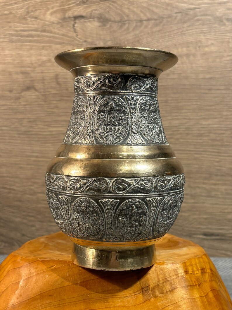 K&ouml;nnte beinhalten: Eine Messingvase mit einem komplizierten, gravierten Design. Die Vase ist dunkelgrau mit goldenen Akzenten. Sie hat einen breiten Boden und einen schmalen Hals.