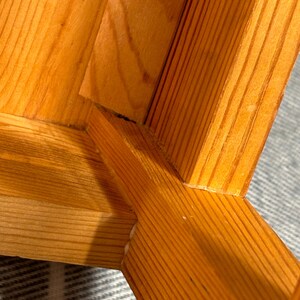 May include: Close-up of a wooden chair's joinery. The chair is constructed from light-colored wood, showcasing the grain and the mortise and tenon joints. The wood has a warm, natural tone.