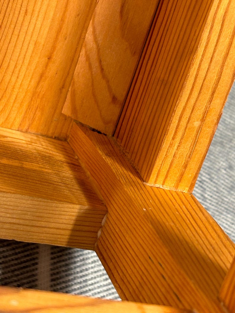 May include: Close-up of a wooden chair's joinery. The chair is constructed from light-colored wood, showcasing the grain and the mortise and tenon joints. The wood has a warm, natural tone.