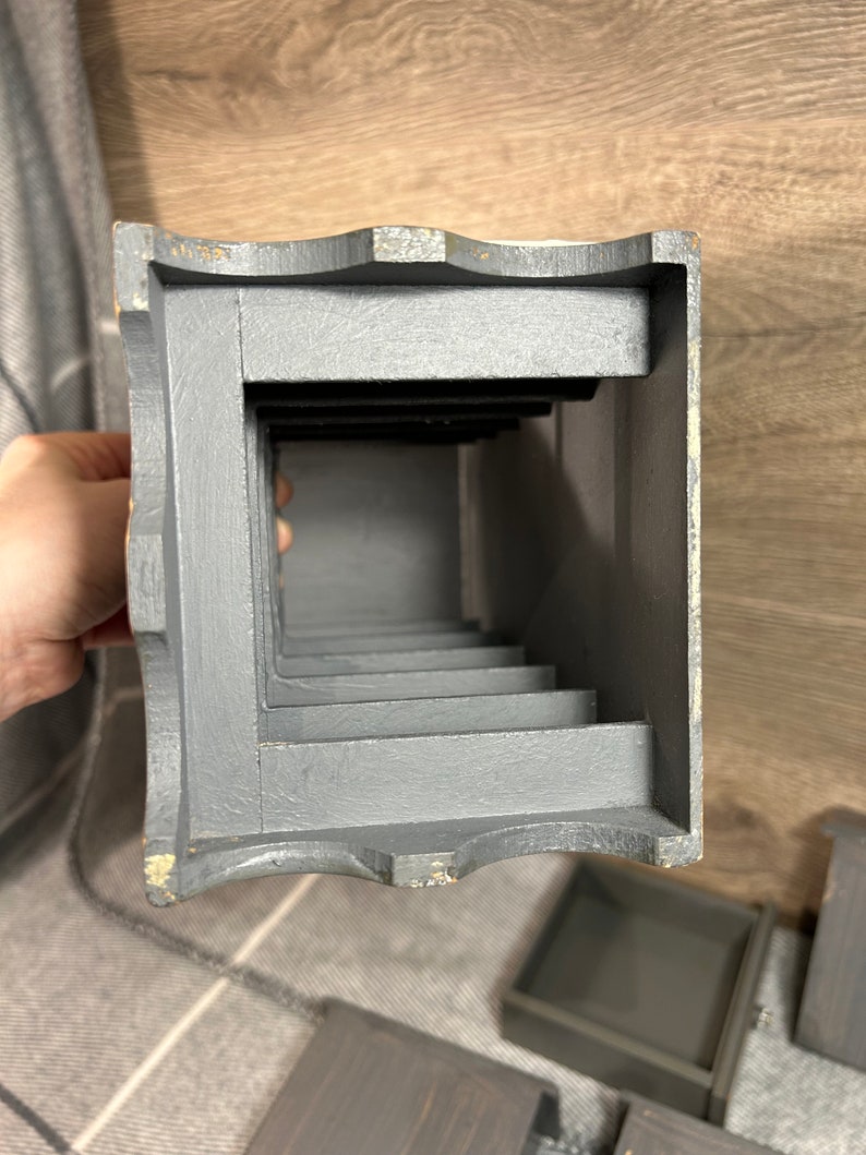 May include: A grey wooden box with a series of compartments. The box is open and the compartments are visible. The box is made of wood and has a rustic look.