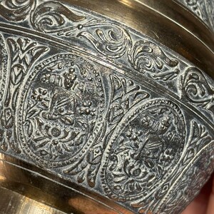K&ouml;nnte beinhalten: Eine Messingvase mit aufwendigen, gepr&auml;gten floralen und geometrischen Mustern. Die Vase hat eine silberfarbene Oberfl&auml;che und einen breiten, runden Boden.