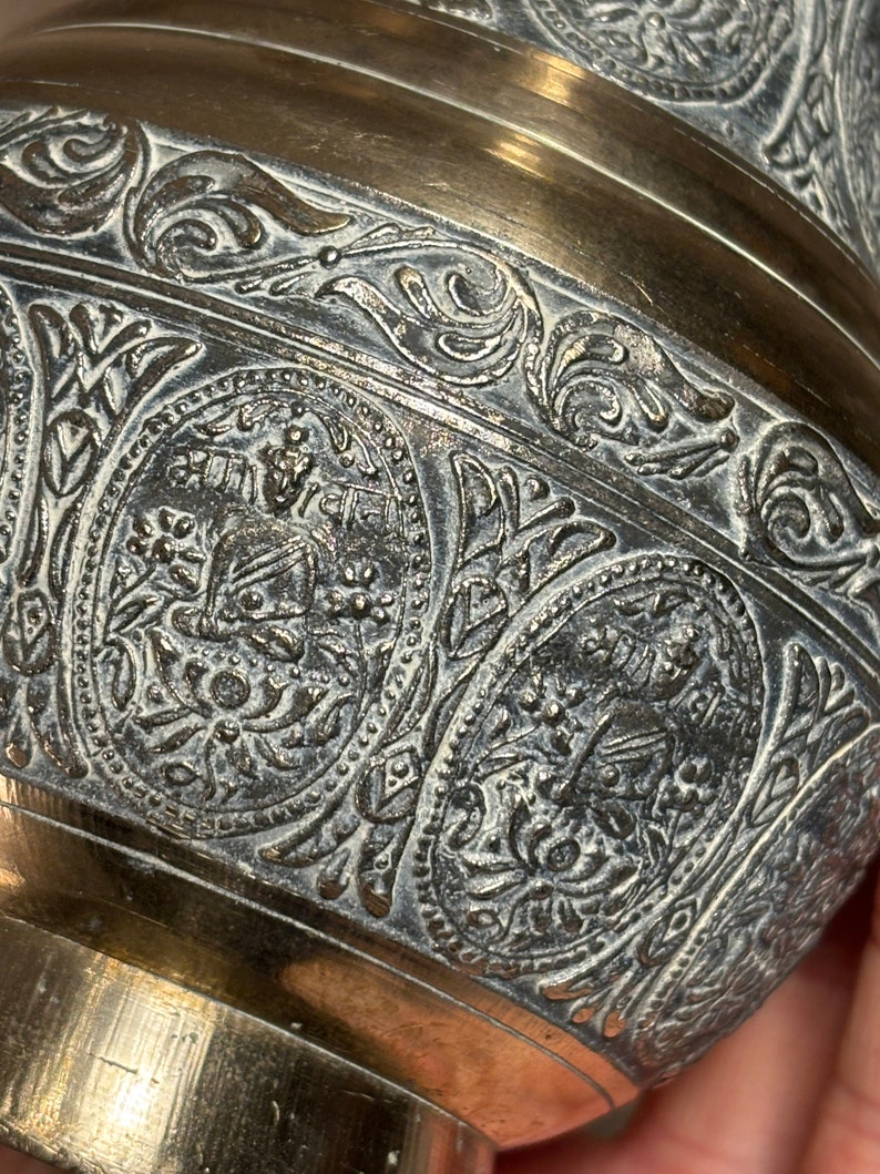 K&ouml;nnte beinhalten: Eine Messingvase mit aufwendigen, gepr&auml;gten floralen und geometrischen Mustern. Die Vase hat eine silberfarbene Oberfl&auml;che und einen breiten, runden Boden.