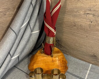 May include: Set of six gold-toned napkin rings on a wooden base with a red napkin with white trim in a holder.