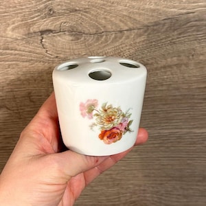 Puede incluir: Portacepillos de dientes de cerámica blanca con cuatro agujeros y un diseño floral con flores rosas, amarillas y naranjas.