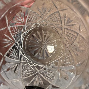 Op de afbeelding: Close-up van een helder glas met ingewikkelde geometrische patronen. Het ontwerp bevat stervormige en rasterachtige vormen, waardoor een textuur ontstaat. Het glas lijkt leeg, met licht dat weerkaatst op het geslepen kristal.