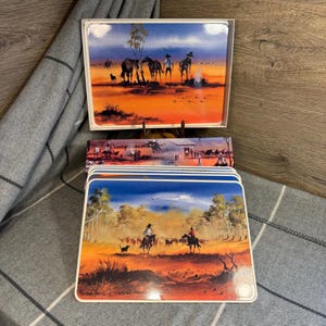 Könnte beinhalten: Satz mit sechs bunten australischen Outback-Platzsets. Jedes Platzset zeigt eine andere Szene mit Cowboys auf Pferden, Rindern und blauem Himmel. Die Platzsets sind aus strapazierfähigem Material gefertigt und perfekt für den täglichen Gebrauch.