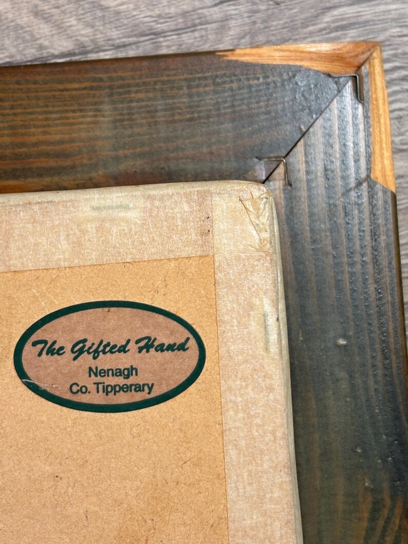 Puede incluir: Primer plano de un marco de imagen de madera marr&oacute;n con una pegatina ovalada verde que dice "The Gifted Hand Nenagh Co. Tipperary".