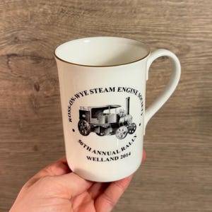 May include: White ceramic mug with a black and white image of a steam engine and the text "Ross-on-Wye Steam Engine Society 50th Annual Rally Welland 2014".