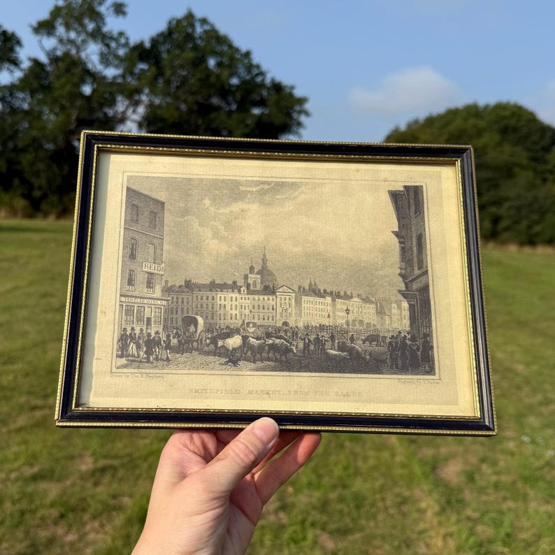 May include: Framed black and gold print of a historical street scene with buildings, people, and horse-drawn carriages. The print is in black and white and has a gold border.
