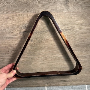 Könnte beinhalten: Ein Vintage-Billardkugel-Rack aus Holz in Dreiecksform. Das Rack besteht aus dunkelbraunem Holz mit einem abgenutzten, gealterten Aussehen. Die Kanten sind abgerundet und das Rack ist für Billardkugeln konzipiert.