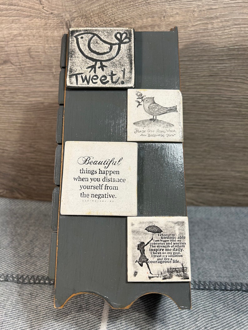 May include: A grey wooden box with a decorative design. The box has a series of square tiles with inspirational quotes and images of birds. The quotes include "Tweet!" "Beautiful things happen when you distance yourself from the negative." "Praise God for the rain, all blessings flow." and "I choose to be unstoppable. I am bigger than my concerns and worries. The strength of others inspire me daily. I focus on my goal. I trust my intuition and live a courageous life."