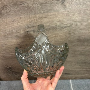 May include: A clear glass bowl with a cut glass design and a handle. The bowl is held in a hand.