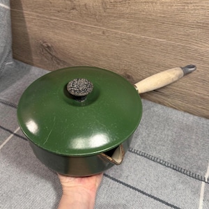 May include: A green enameled saucepan with a lid and a wooden handle. The lid has a black and gray knob. The saucepan has a spout for pouring. The handle is approximately 6 inches long.