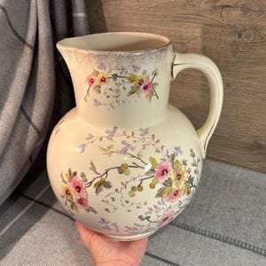 Może przedstawiać: Zestaw trzech ceramicznych kubków z nakrapianym, matowym wykończeniem. Kubki są w odcieniach kremu, jasnoszarym i ciemnoszarym. Każdy kubek ma prosty, minimalistyczny design, idealny do kawy lub herbaty.
