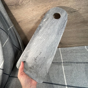 Puede incluir: Una bandeja de servir rectangular de mármol gris con un agujero en el asa. La bandeja es rectangular y tiene una superficie lisa.