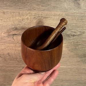 May include: A wooden mortar and pestle set. The mortar is a round, dark brown bowl with a smooth finish. The pestle is a matching color and has a rounded handle. The set is designed for grinding herbs and spices.